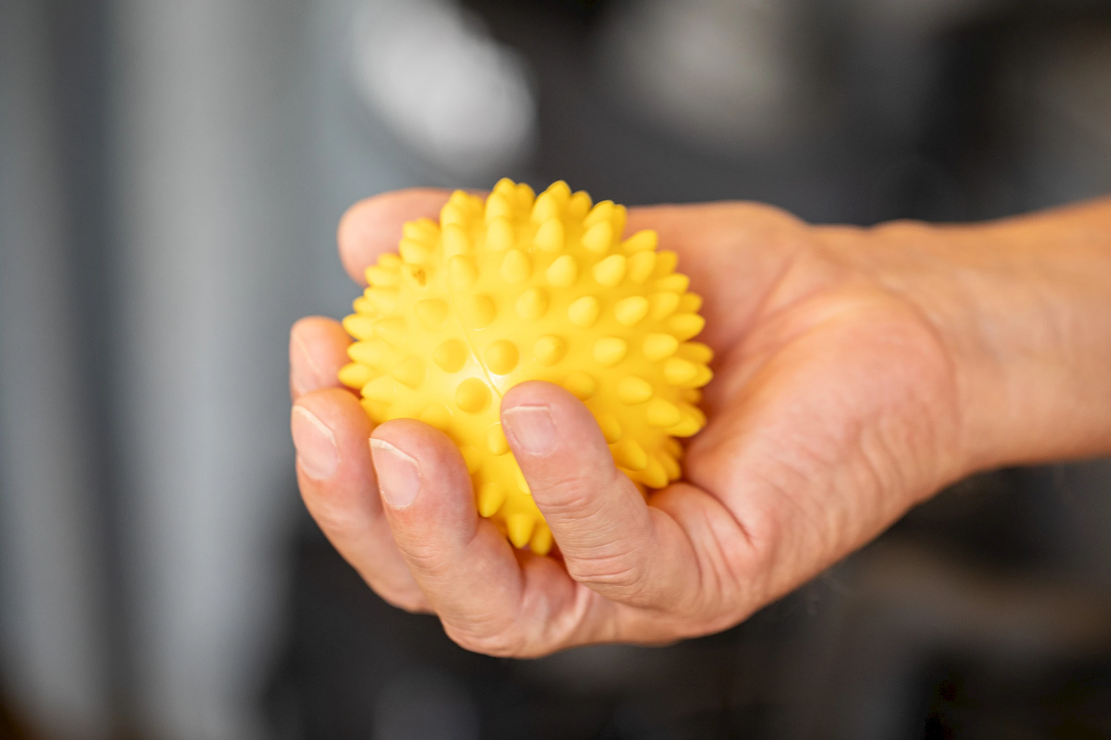 Hand hält einen gelben Igelball zur Handtherapie